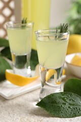 Tasty limoncello liqueur and green leaves on light textured table, closeup