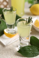 Fototapeta premium Tasty limoncello liqueur and green leaves on light textured table, closeup