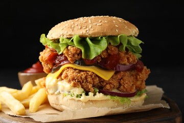 Delicious burger with crispy chicken patty, french fries and sauce on black table, closeup