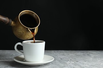 Turkish coffee. Pouring brewed beverage from cezve into cup at grey table. Space for text
