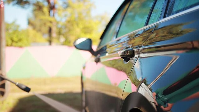 Washing a gray car outdoors in summer with a mini high-pressure washer. A jet of water under pressure washes away dirt on a car. Slow motion