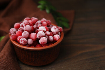 Frozen red cranberries in bowl on wooden table, closeup. Space for text