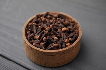 Aromatic cloves in bowl on grey wooden table, closeup