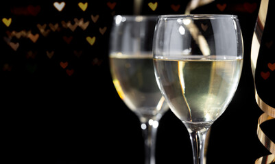 White wine glasses heart bokehs on black background. Special day celebration background. For...