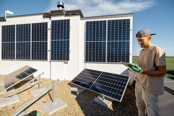 Technician with a digital tablet checks the operation of a newly installed solar station on the roof of a house. The concept of maintenance of solar plants and their performance - obrazy, fototapety, plakaty