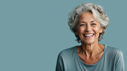 A joyous senior woman with silver hair laughing heartily, her happiness radiating in the warm light against a soft blue background - obrazy, fototapety, plakaty