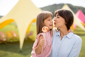 Obraz premium Portrait of happy mom with little girl visit an amusement park, spending summertime happily together. Concept of parenthood, entertainment and summer vacation