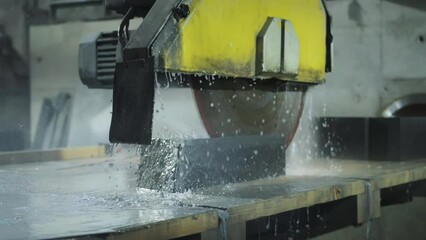 A large modern machine with a circular saw that cuts a large porcelain stoneware stone. Production of finishing plates from porcelain stoneware for stairs, industry. Slow motion