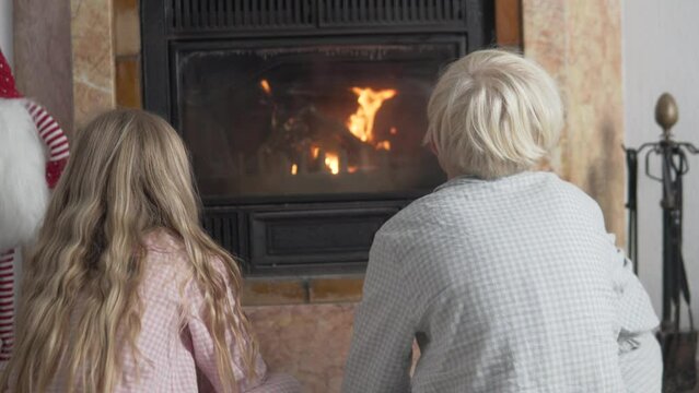 Boy and girl warming themselves by the fireplace in winter, children sitting next to the fireplace and looking at the fire