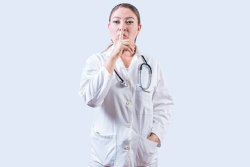 Female doctor making silence gesture isolated. Beautiful female doctor silencing and looking at the...