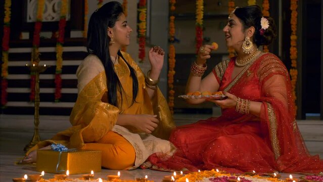 Diwali celebration - Mother feeding laddoo to her daughter (Duo in traditional dress and jewellery). 