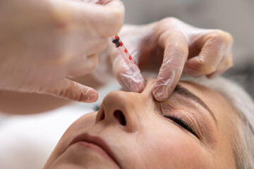 Beautician injecting filler into forehead of a female patient