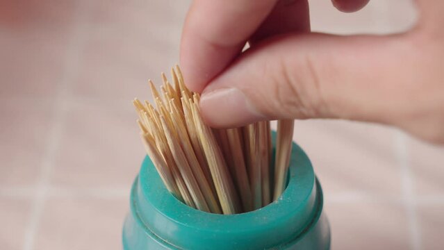 Hand picking up a wooden toothpick from a canister. Close up