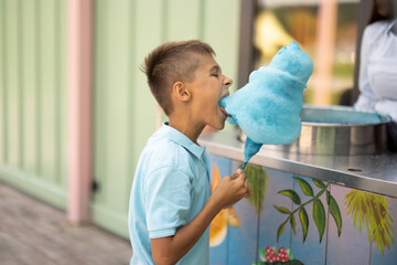 Happy boy eats blue cotton candy while visiting amusement park, spending summertime happily,...