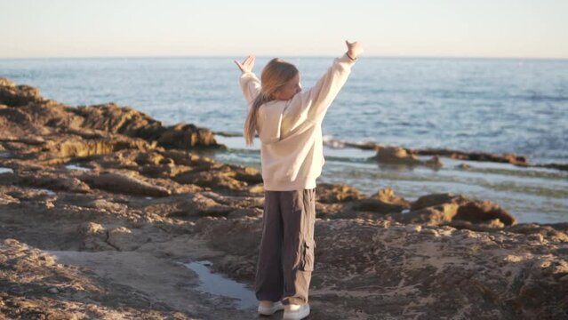 Little blonde girl soaking her hands up by the sea, wild beach at sunse