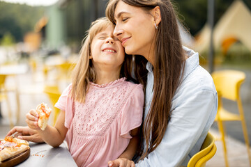 Cheerful mom with her little daughter eating pizza outdoors, visiting amusement park during a...