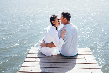 Young couple in love in light casual clothes is sitting on wooden bridge