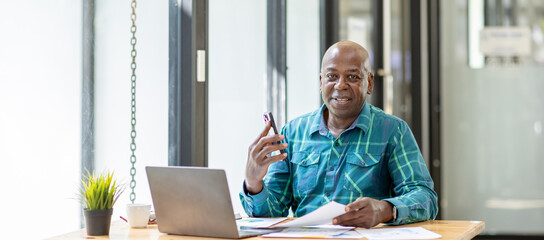 Portrait of Senior African man sitting on laptop at the home office and having a phone conversation with the insurance company.
