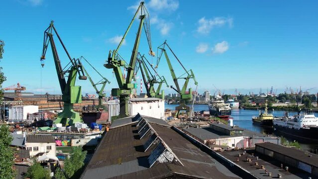 Shipyard cranes aerial view. Establishing shot of shipyard by the Baltic sea in Gdansk, Poland, Europe. Industrial seaside scene, ships in the harbor and dry dock.