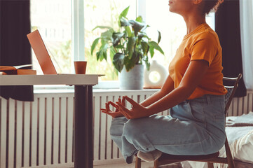 Stress relief and freelance. African american female freelancer sitting in lotus pose and meditating