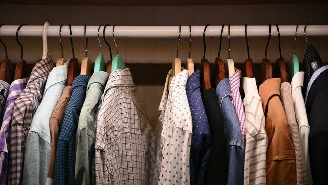 Hangers inside male wardrobe with many shirts and jackets. Unrecognisable man takes a red shirt from the closet
