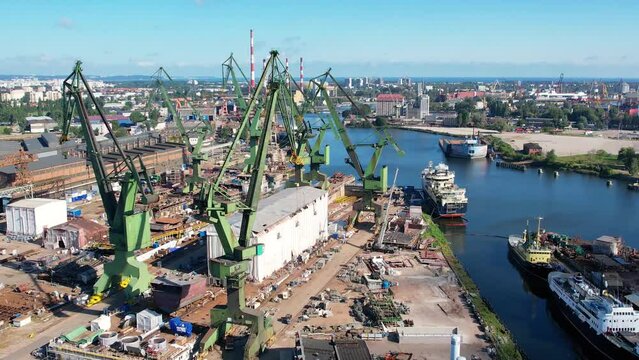 Shipyard cranes aerial view. Establishing shot of shipyard by the Baltic sea in Gdansk, Poland, Europe. Industrial seaside scene, ships in the harbor and dry dock.