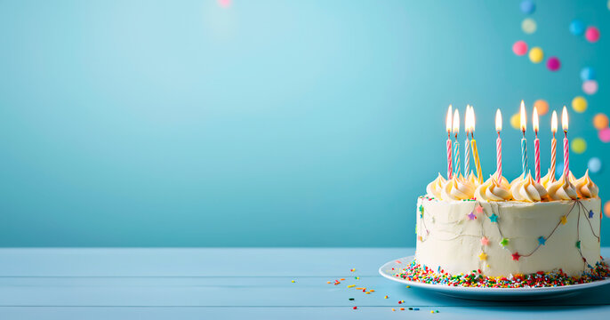 Festive birthday cake with lit candles and colorful sprinkle. Isolated on a blue background with copy space.
