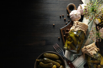Canned cucumbers in a jar, with ingredients on a dark table.