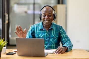 Portrait of happy African American senior man 60 years old  wearing headphones, enjoying working at...