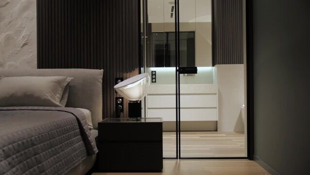 Close-up luxury bedroom interior design and decoration with grey bedding sheet and blanket, bad table with modern lamp light turned on and cabinet with mirror doors, dolly shot slow motion.