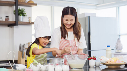 Young asian mother and little daughter enjoy cooking together in kitchen room at home. A little girl helping mother preparation baking in holidays. Mother and daughter prepare dough, bake cookies