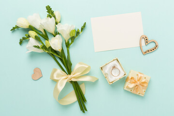 White freesia flower and gift box with diamond ring on color background, top view