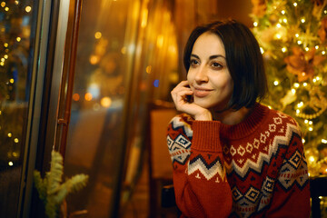 Merry Christmas woman portrait. Girl in red knitted sweater at cozy festive cafe in Christmas eve