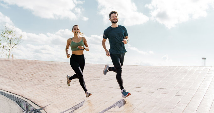 Joyful couple running on a rooftop, clear blue sky above and city horizon in view.