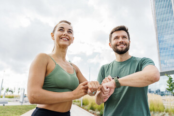 Smiling couple checking fitness progress on smartwatch after workout, urban park.