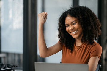 Successful business woman, excited young woman Keeping up arms and showing positive emotions, happy working in modern office on Tablet and computer.
