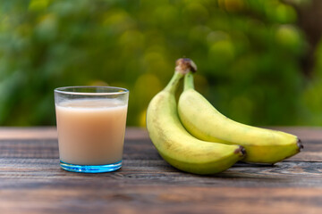 banana juice in blue glass cup on a wooden table on a green blurred background of nature