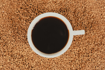 A cup of hot instant coffee on a background of freeze-dried granules