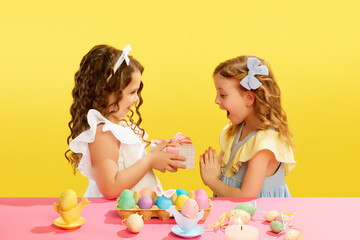 Little girl presenting to her friend a gift, box, Easter present against yellow background. Celebration, presents. Concept of Easter holiday, celebration, traditions, childhood, happiness