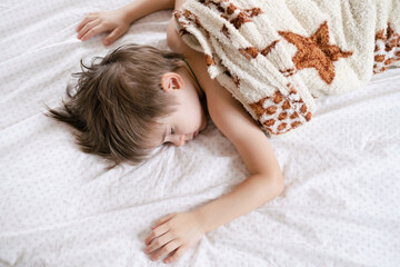 Cute little toddler boy is sleeping with beige plaid at home. Bedtime, napping