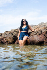 Beautiful woman wearing sunglasses leaning against rocks on a beach.