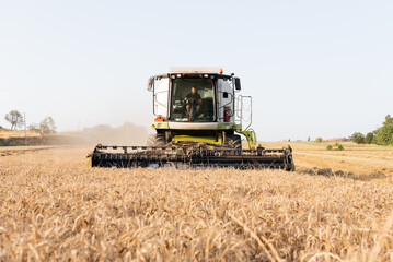 Frontal view of young farmer driving combine harvester with header on dry wheat field