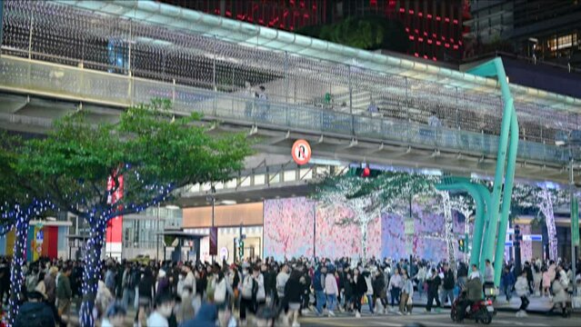 Blurred scene of pedestrians crossing the sidewalk at a busy intersection. People preparing for New Year's Eve and shopping in Xinyi District, Taipei.