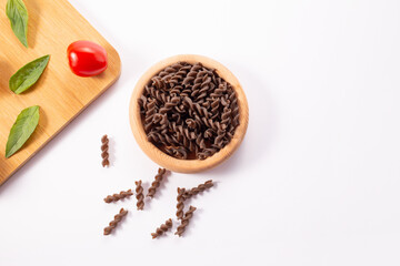 Organic uncooked Buckwheat Fusilli pasta, tomatoes cherry and basil leaf, on white background. Wholegrain gluten free noodles. Healthy food concept