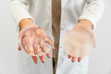 Doctor's hands holding two different types of breast prostheses.