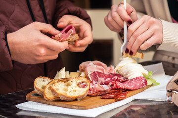 Obraz na płótnie Canvas Couple of tourists eating a mixture of cured meats, cheese, mozzarella with slices of local crunchy white bread placed on a wooden board in a food street market