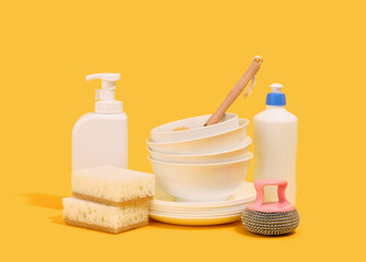 Clean dishes and dishwashing detergent. Dish washing supplies on a yellow background.
