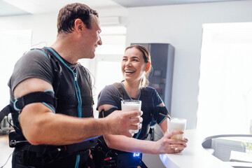 Young smiling man and woman in ems suits communicate and drink protein shakes in sports bar