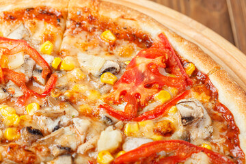 delicious pizza with chicken, mushrooms, cheese, tomatoes and corn on a wooden background
