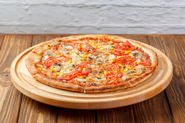 delicious pizza with chicken, mushrooms, cheese, tomatoes and corn on a wooden background